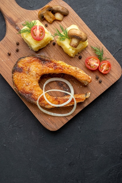 Vue verticale de délicieux repas de poisson frit et champignons tomates verts sur une planche à découper en bois sur une surface noire