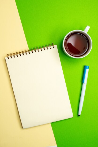 Vue verticale du cahier blanc avec stylo à côté d'une tasse de thé sur fond blanc et jaune