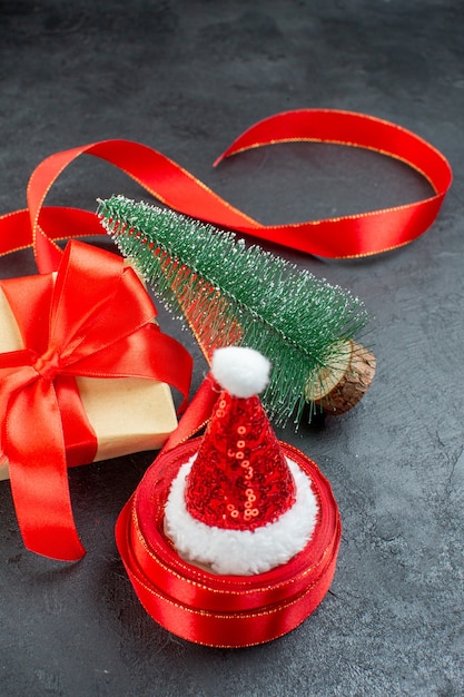 Vue verticale du chapeau de père Noël sur un rouleau de ruban et beau cadeau arbre de Noël sur fond sombre