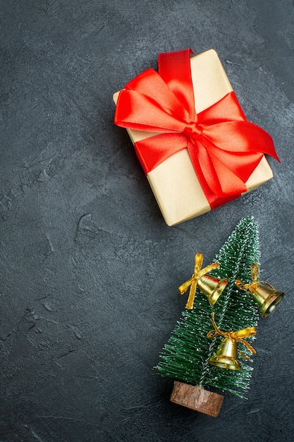Vue verticale du coffret cadeau avec ruban rouge en forme d'arc et arbre de Noël décoré o fond noir