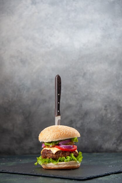 Vue verticale du couteau dans un délicieux sandwich sur plateau noir sur une surface grise floue isolée