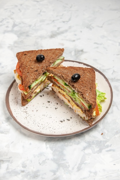 Vue verticale du délicieux sandwich avec du pain noir décoré d'olives sur une plaque sur une surface blanche tachée