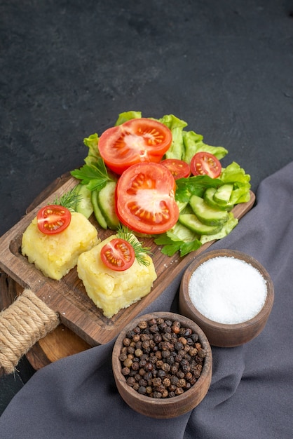 Vue verticale du fromage de légumes frais hachés sur une planche à découper et épices sur une serviette de couleur foncée sur une surface noire