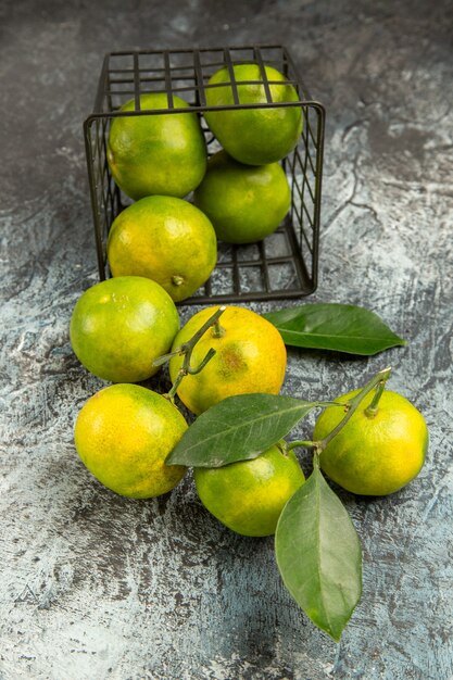 Vue verticale du panier tombé avec des mandarines vertes fraîches coupées en deux et des mandarines pelées sur fond gris