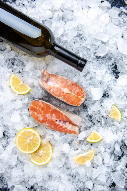 Photo gratuite vue verticale du poisson frais divisé en deux parties avec des tranches de citron et une bouteille de vin sur des glaces