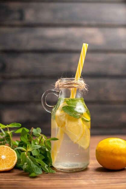 Vue verticale de l'eau de désintoxication fraîche servie avec de la menthe en tube et de l'orange sur fond marron