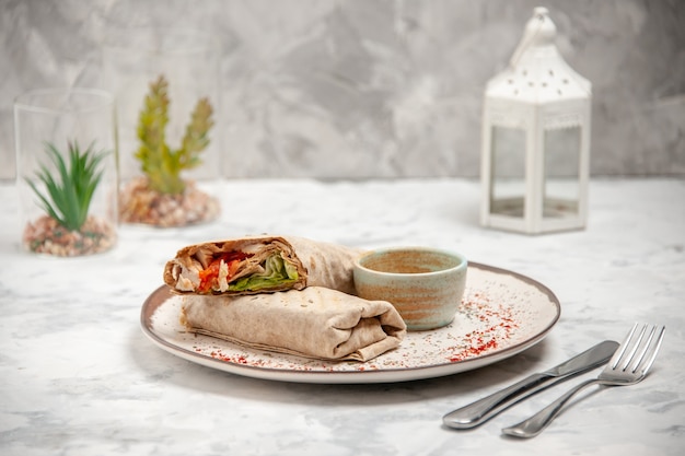 Vue verticale de l'enveloppe de lavash et du yogourt dans un petit bol sur une assiette et des couverts de maison de jouets sur une surface blanche tachée