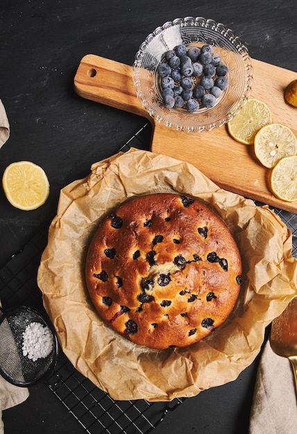 Vue verticale d'un gâteau aux cerises avec du sucre en poudre et des ingrédients sur le côté sur un fond noir