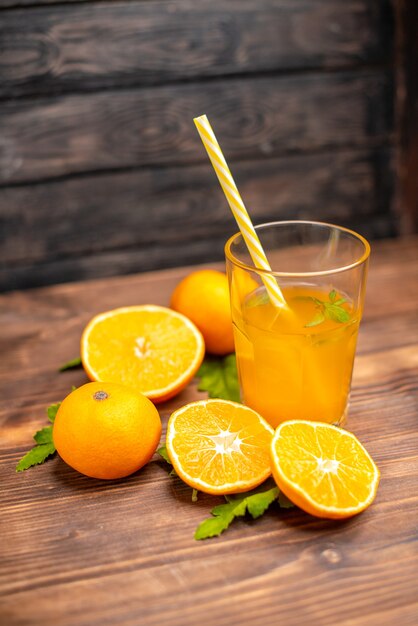 Vue verticale de jus d'orange frais dans un verre servi avec de la menthe en tube et des oranges entières coupées sur le côté gauche sur une table en bois