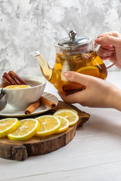 Vue verticale de la main tenant la théière du thé noir dans une tasse blanche autour du thé sec et des feuilles sur un tableau blanc