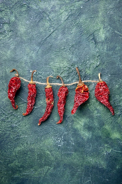 Vue verticale de poivrons rouges séchés attachés avec une corde sur fond de couleurs mélangées noir vert