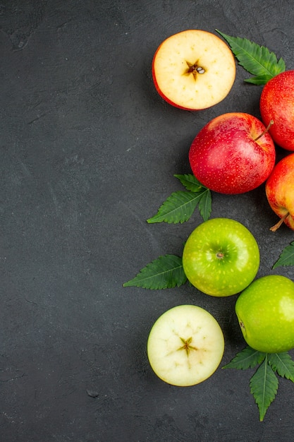 Vue verticale des pommes rouges fraîches entières et coupées et des feuilles sur le côté gauche sur fond noir