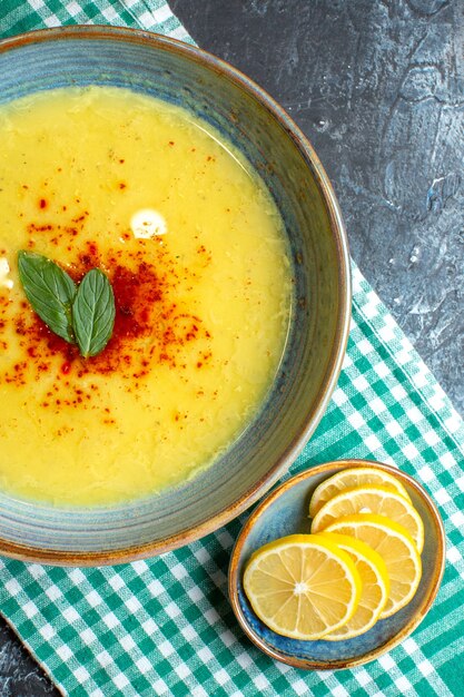 Vue verticale d'un pot bleu avec une soupe savoureuse servie avec de la menthe et du citron haché sur une serviette dénudée verte à moitié pliée sur fond bleu