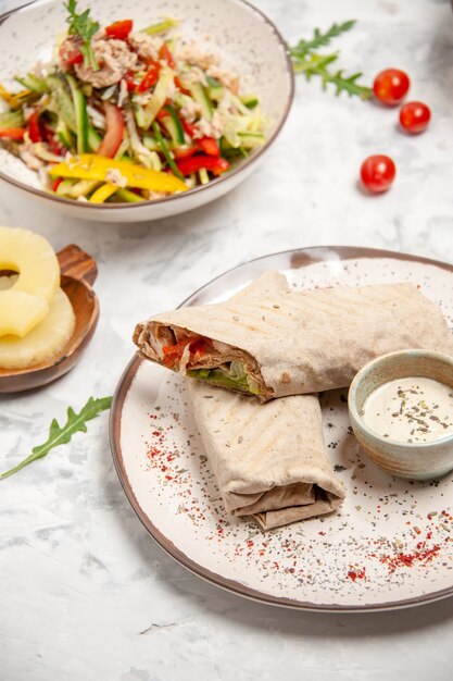 Vue verticale de salades végétaliennes saines ananas séchés et enveloppements lavash sur surface blanche tachée