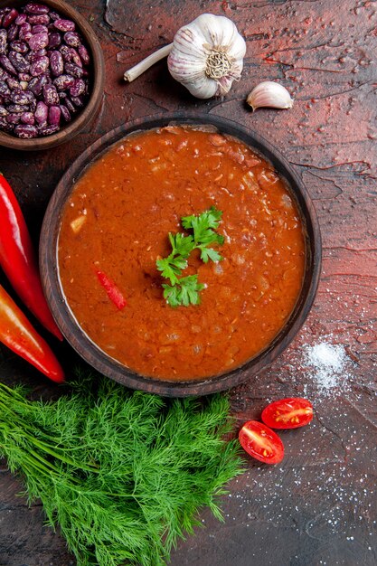 Vue verticale de la soupe aux tomates dans un bol brun et différentes épices ail citron sur table de couleurs mixtes