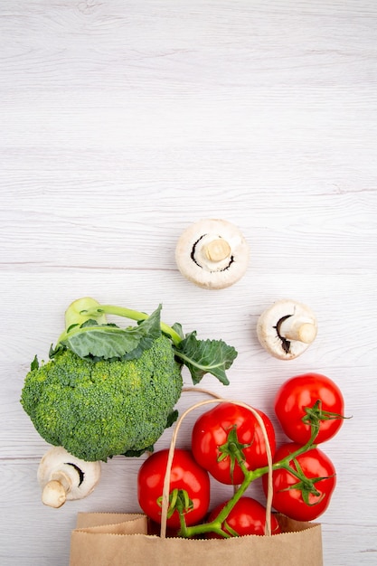 Vue verticale des tomates fraîches avec le brocoli de champignons de tige dans un panier sur le fond blanc