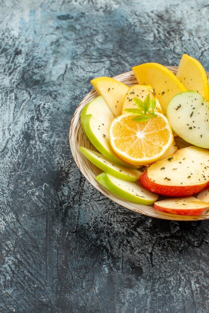 Vue verticale de tranches de pomme rouge vert jaune frais sur une plaque blanche avec du citron sur le côté gauche sur fond gris