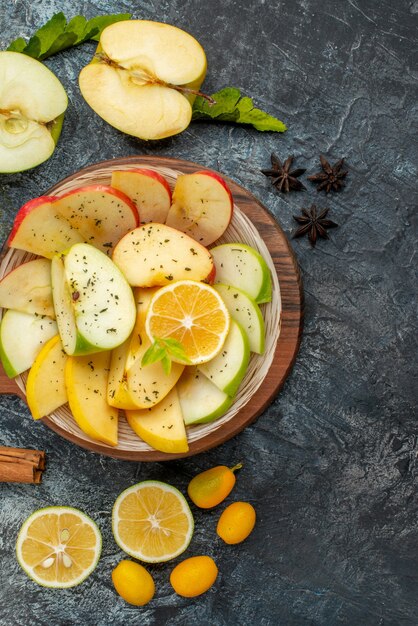 Vue verticale de tranches de pommes fraîches sur une plaque blanche avec du citron sur une planche à découper en bois sur fond gris