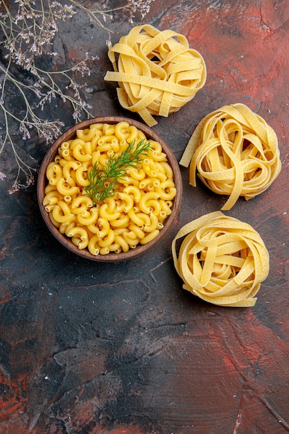 Photo gratuite vue verticale de trois pâtes spaggeties et papillons non cuits dans un bol brun et vert sur fond de couleur mixte