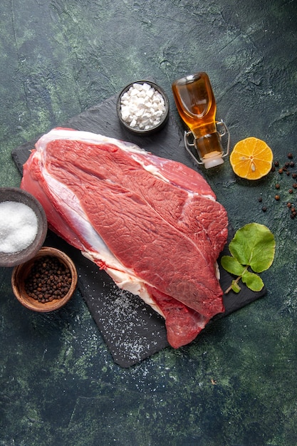 Vue verticale de la viande rouge crue fraîche sur le plateau noir bouteille d'huile tombée citron poivre sur fond de couleur sombre