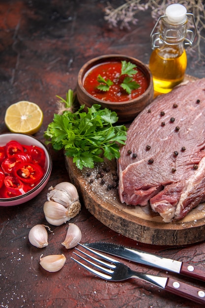 Vue verticale de la viande rouge sur un plateau en bois et du ketchup vert à l'ail et une bouteille d'huile de poivre hachée sur fond sombre image stock