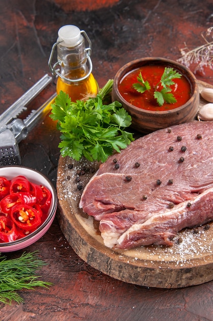 Vue verticale de la viande rouge sur un plateau en bois et du ketchup vert à l'ail et une bouteille d'huile de poivre hachée sur fond sombre