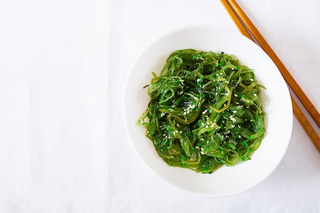 Wakame Chuka ou salade d'algues aux graines de sésame dans un bol sur un tableau blanc. Cuisine japonaise traditionnelle. Vue de dessus. Mise à plat