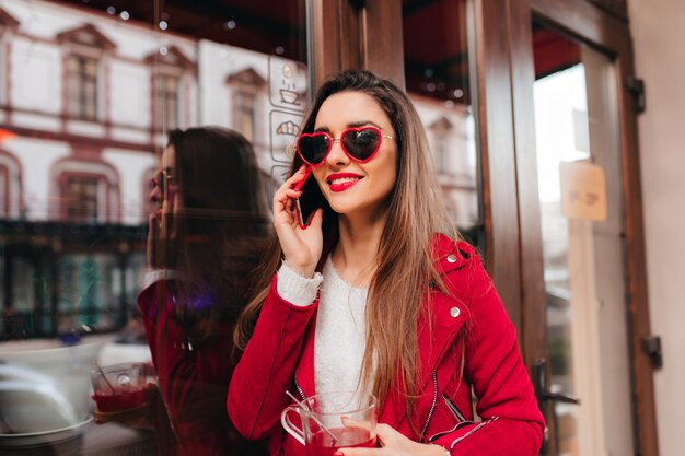 Winsome dame aux cheveux bruns, parler au téléphone près de café