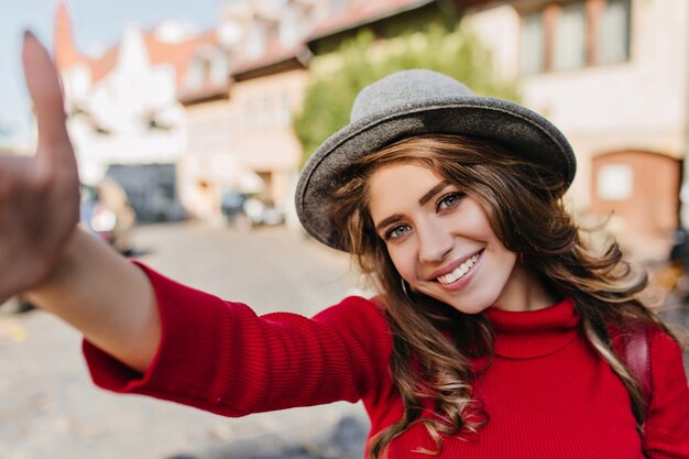 Winsome femme blanche en pull tricoté faisant selfie en marchant sur l'avenue