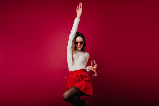 Winsome girl en jupe rouge courte danse drôle avec verre à vin à la main