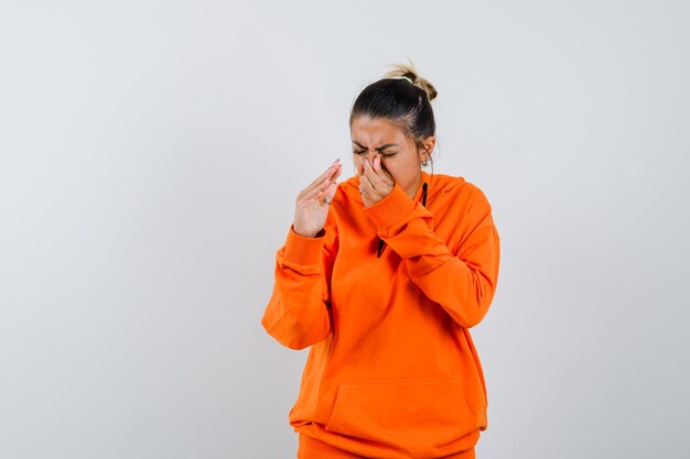 Woman in orange hoodie pinçant le nez à cause d'une mauvaise odeur et ayant l'air dégoûté