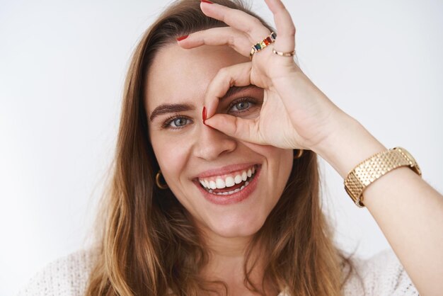 Woman smiling rester positif montrant ok ok geste regardant à travers souriant joyeusement s'amusant à profiter des rayons de soleil du printemps