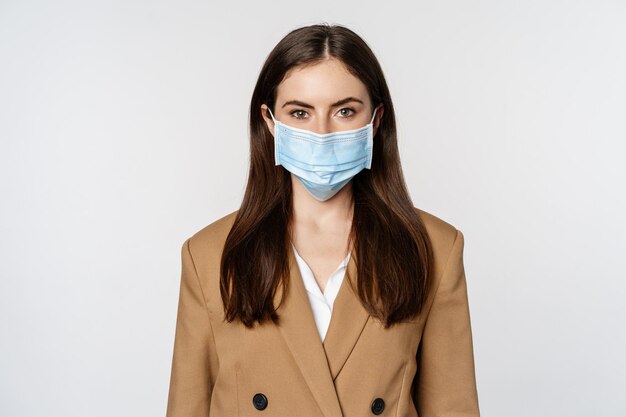 Workaplce et concept de pandémie. Portrait de visage d'une femme d'affaires portant un masque médical et un costume, regardant sérieusement la caméra, allant travailler pendant covid-19