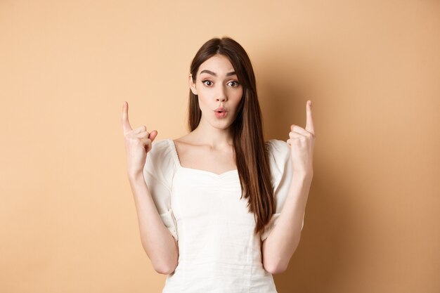 Wow regarde une jeune femme intriguée montrant une offre intéressante en pointant les doigts vers le haut et a l'air excitée debout...