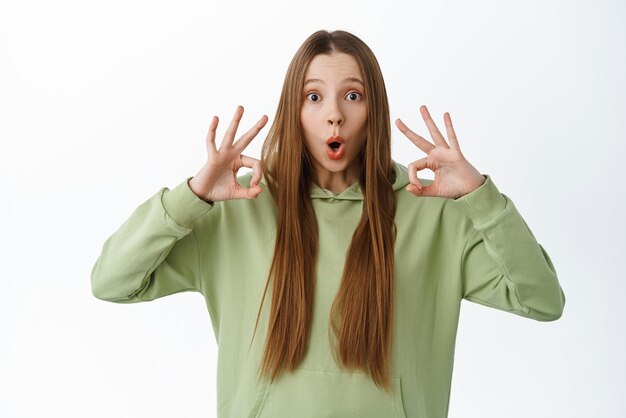 Wow so cool Une jeune femme impressionnée qui montre un signe correct Un geste OK fasciné par la caméra réagit à une publicité super cool debout sur fond blanc