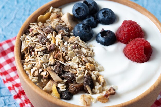 Yaourt aux baies et muesli pour le petit déjeuner dans un bol sur fond lbue