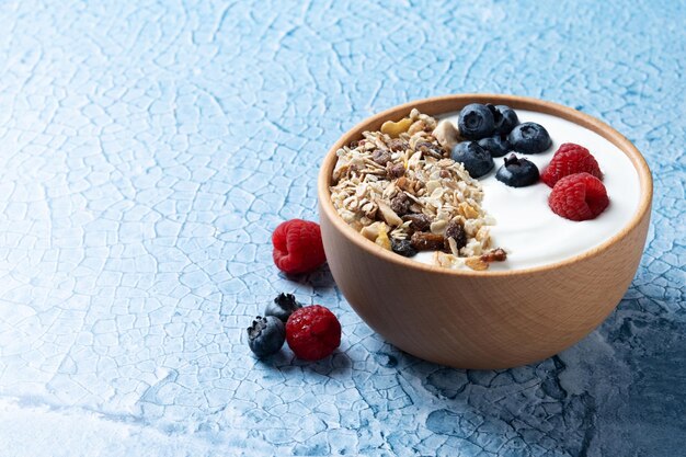 Yaourt aux baies et muesli pour le petit déjeuner dans un bol sur fond lbue