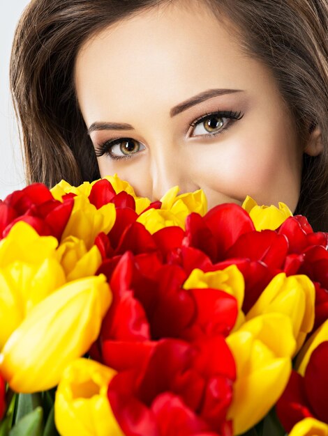 Yeux de belle femme parmi les fleurs. Portrait d'une jolie fille couvre le visage avec des tulipes rouges et jaunes