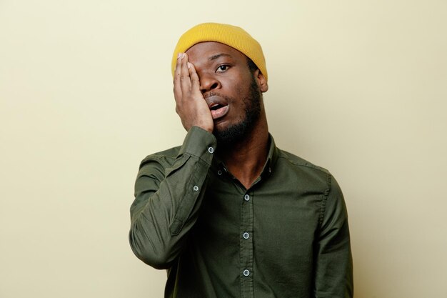 Yeux couverts confus jeune homme afro-américain en chapeau portant une chemise verte isolée sur fond blanc