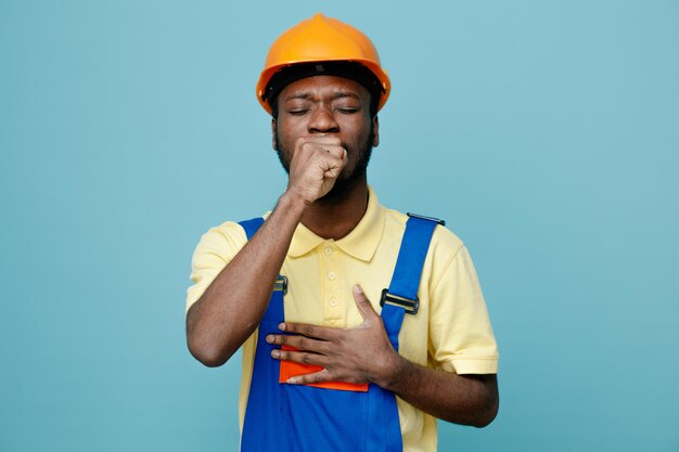 Les yeux fermés attrapant un jeune constructeur afro-américain en uniforme isolé sur fond bleu