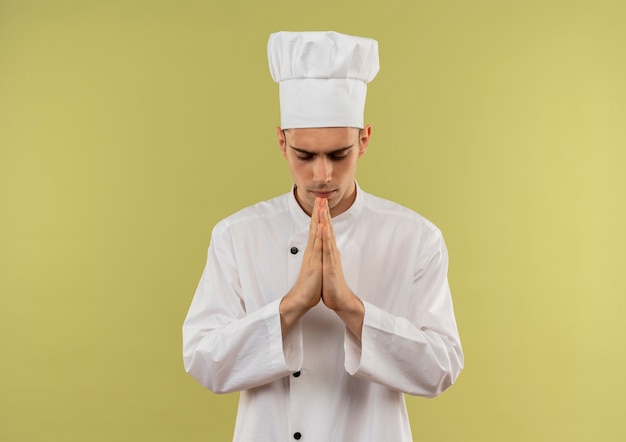 Avec les yeux fermés jeune cuisinier mâle portant l'uniforme de chef montrant le geste de prier avec copie espace