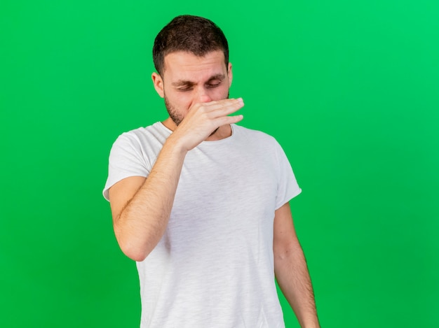 Photo gratuite avec les yeux fermés jeune homme malade essuyant le nez avec la main isolé sur fond vert