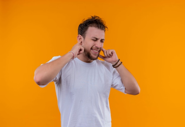 Avec les yeux fermés jeune homme portant un t-shirt blanc oreilles fermées sur mur orange isolé