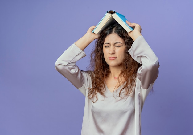 Avec les yeux fermés jeune jolie fille tête couverte de livre isolé sur mur bleu