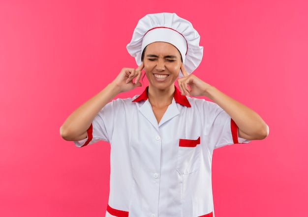 Photo gratuite avec les yeux fermés souriant jeune femme cuisinier portant l'uniforme de chef oreilles fermées avec copie espace