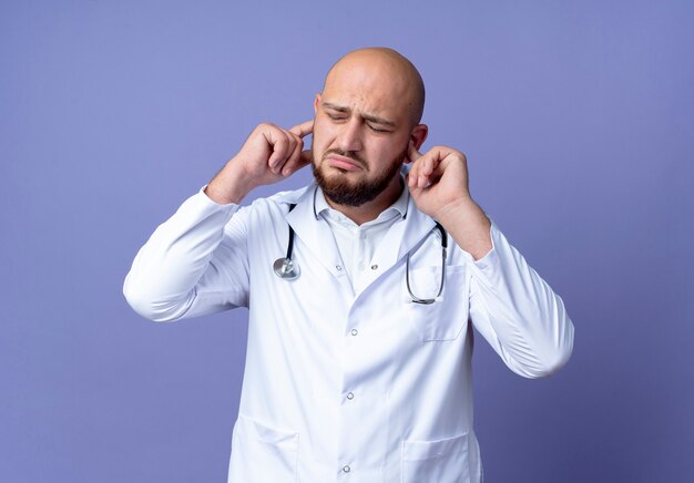 Avec les yeux fermés triste jeune médecin de sexe masculin chauve portant une robe médicale