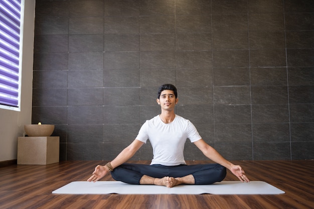 Yogi indien assis et tenant les pieds ensemble dans une salle de sport