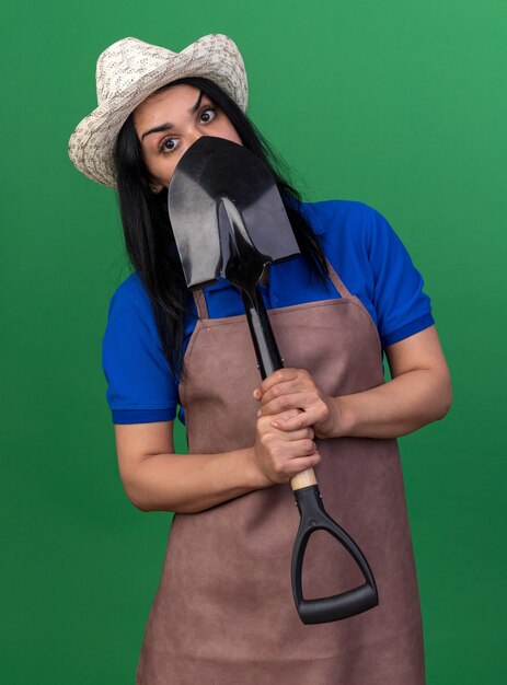 Young caucasian gardener woman wearing uniform and hat holding spade par derrière