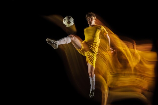 Young caucasian male football ou soccer player kick ball for the goal in mixed light on dark wall concept of Healthy lifestyle professional sport hobby