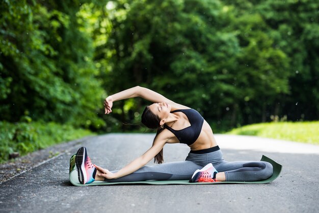 Young fitness woman runner stretching jambes avant de courir dans le parc de la ville